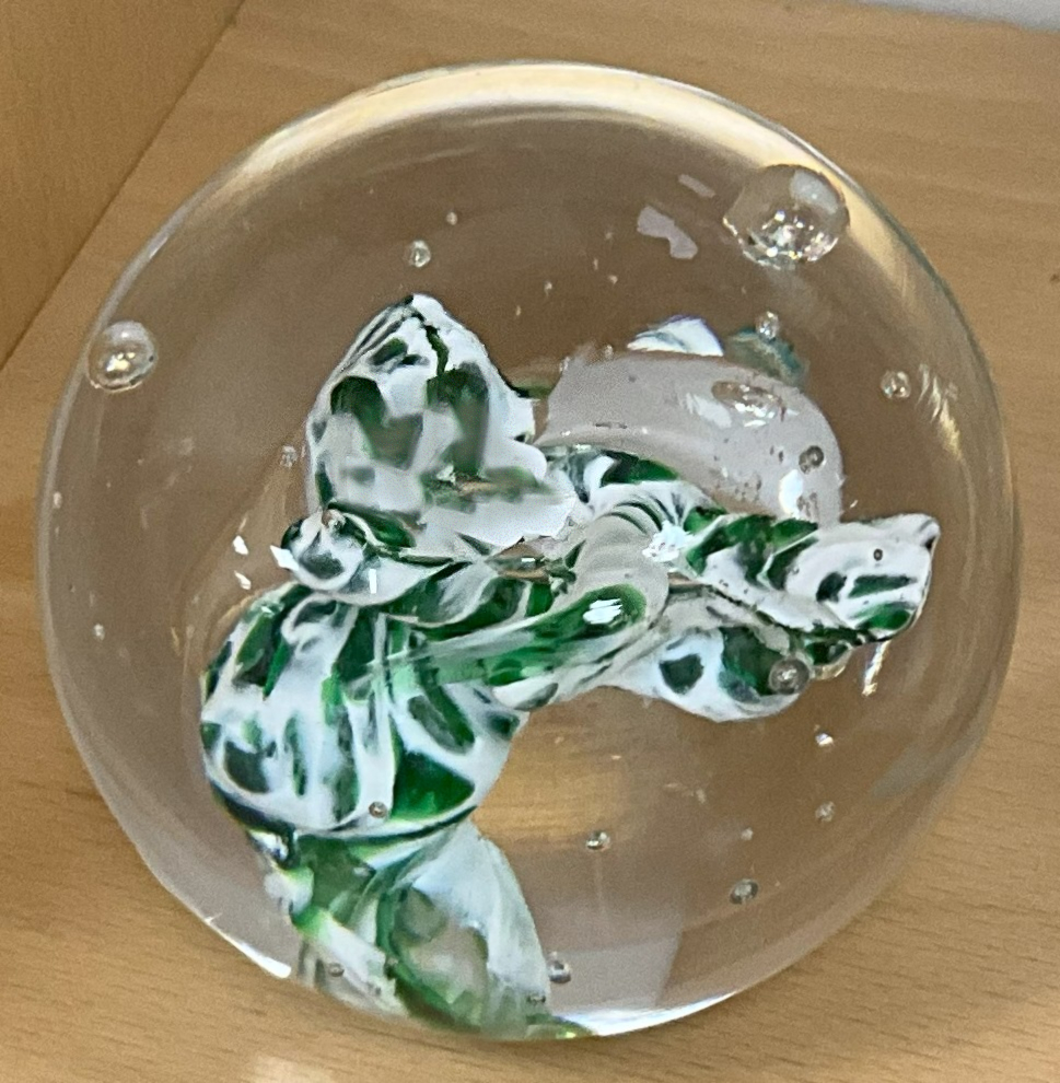 A spherical hand-blown glass paperweight in the French sulfure tradition, containing delicate internal decorations resembling seaweed or flowers.