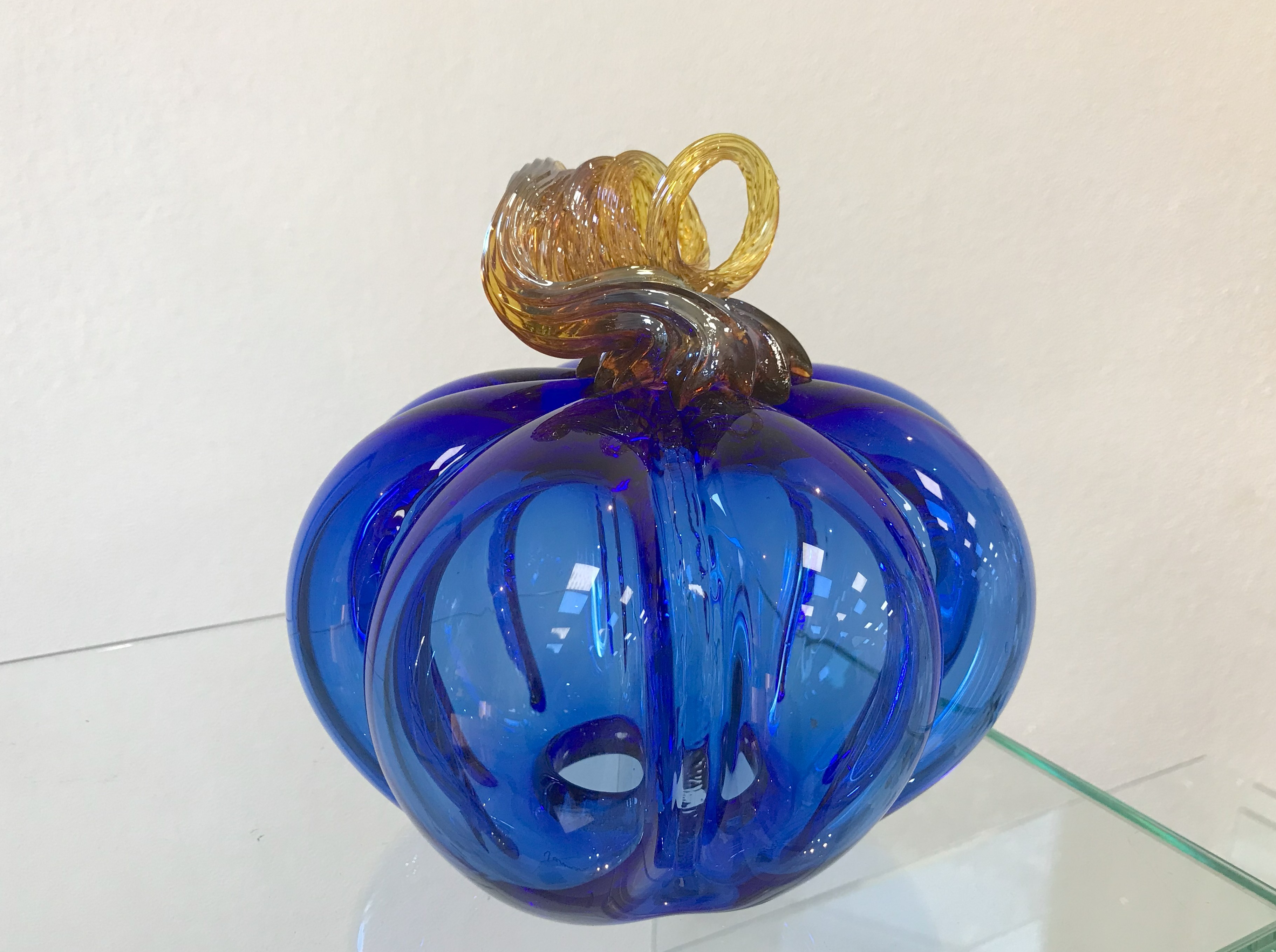 Citrouille en verre soufflé présentée dans un décor d’automne ou d’intérieur, doucement illuminée de l’intérieur.